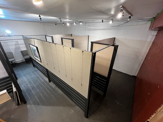 A sparsely furnished workshop or studio with partitions and a gray floor, featuring various light sources and shadows indi...